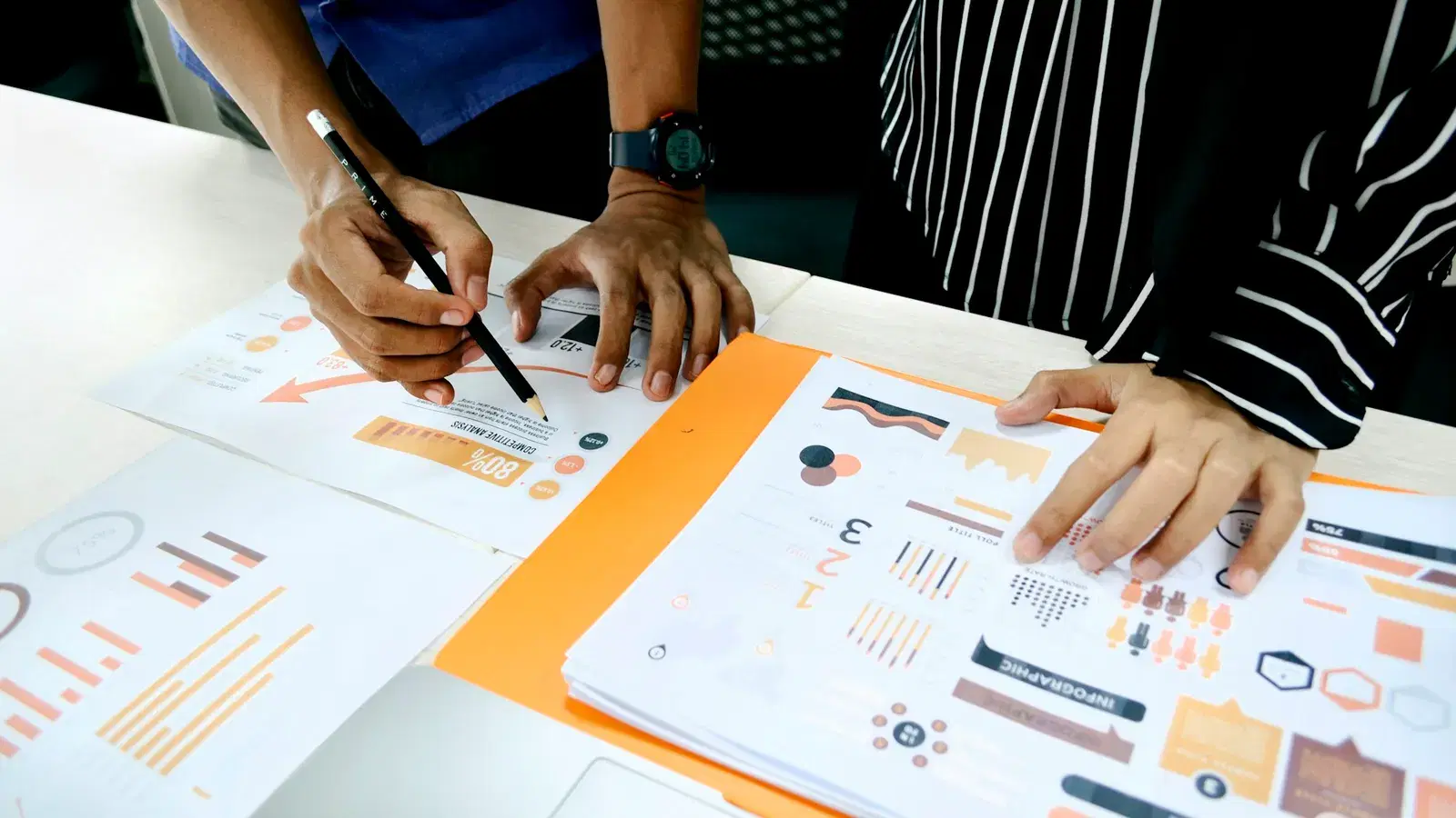 Two colleagues reviewing printed performance charts and infographics on a desk